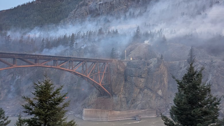 A bridge over a river in the mountains surrounded by smoke.