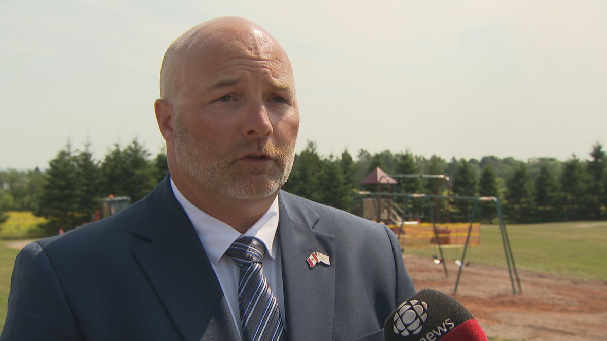A man in suit and tie. Behind him is a playground.