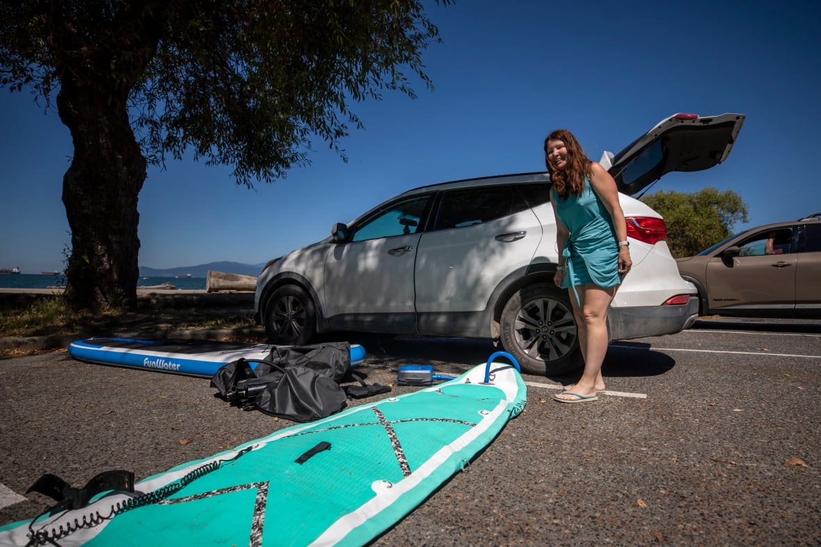 Una mujer con ropa azul eleva un pájaro de pie al lado del SUV blanco, que se detiene en la playa.