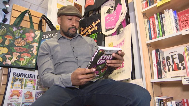 Khodi Dill sits in front of a shelves filled with books as he holds his novel Stay Up.
