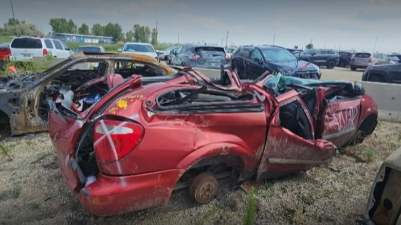 The wreckage of a red minivan that has had its roof caved in windows smashed and sides spray-painted. 