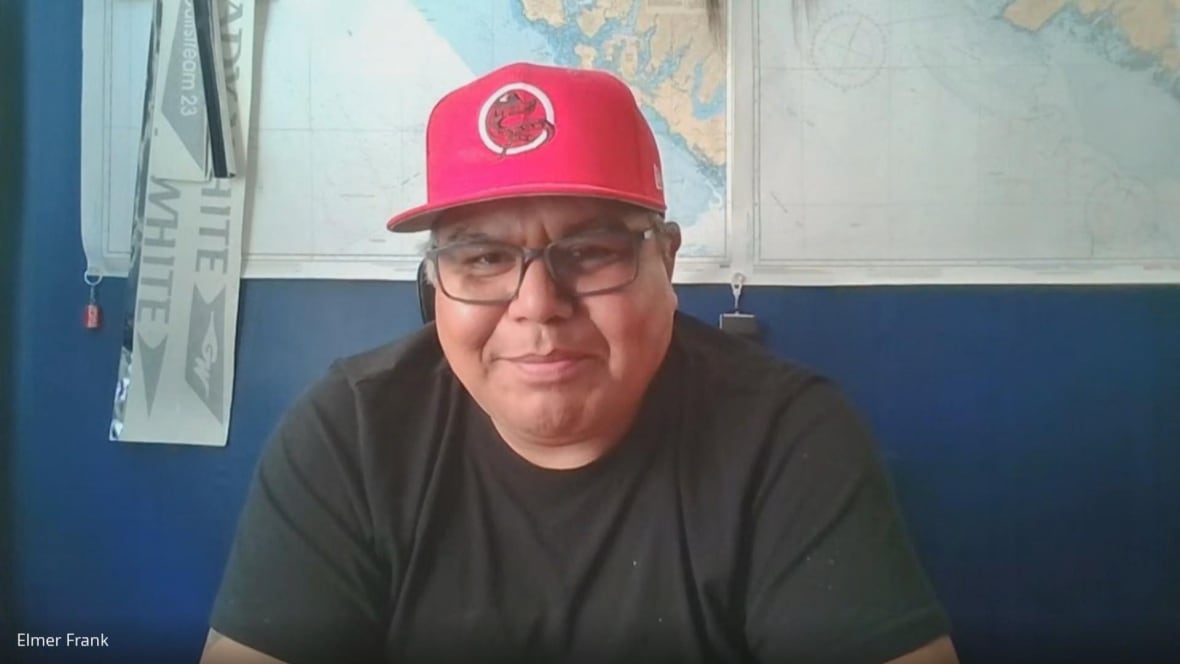 A man wearing a red hat smiles in front of a map.