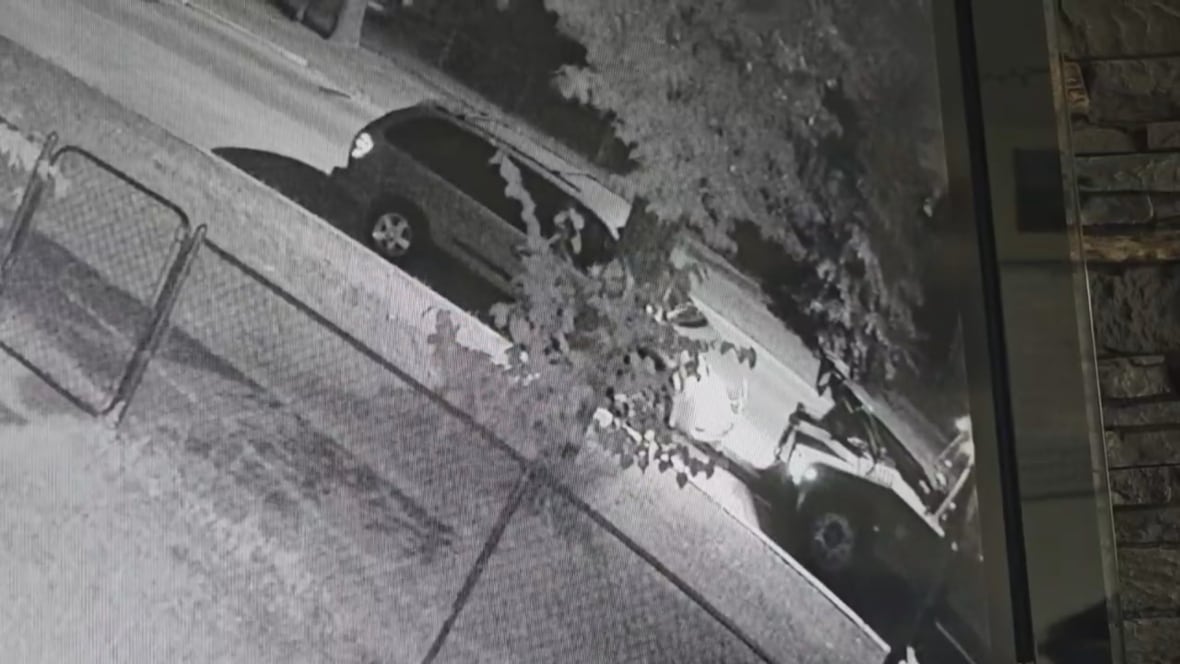 Black and white image of a minivan hooked up to a tow truck on a residential street at night time. 