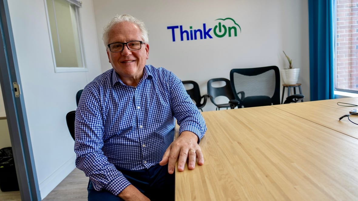 A man sits in a boardroom with the words ThinkOn behind him.