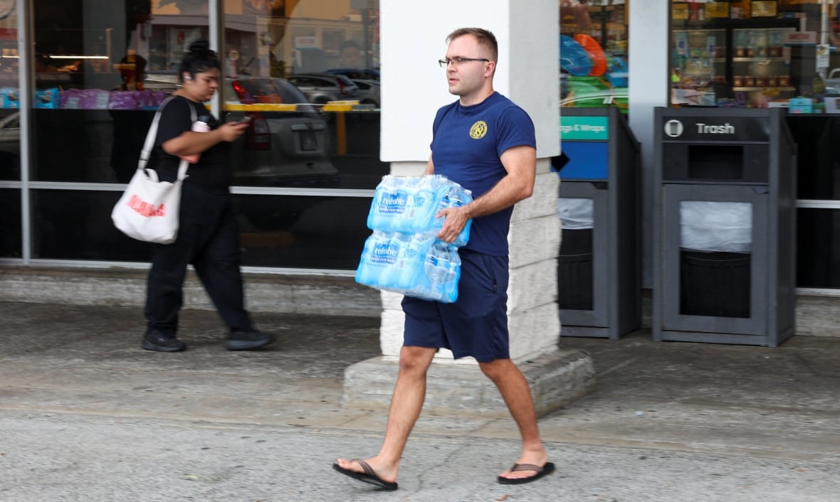 A man carries a large water cooler out of a grocery store. 