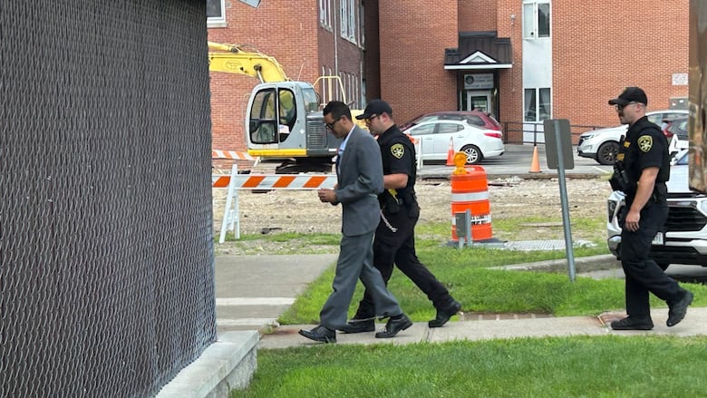 man in suit being escorted by cop. 