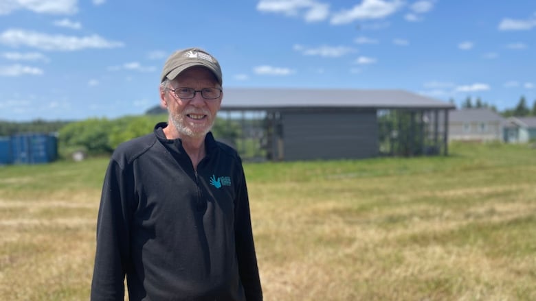 Man with a ball cap and black long sleeve shirt standing before a wildlife enclosure.