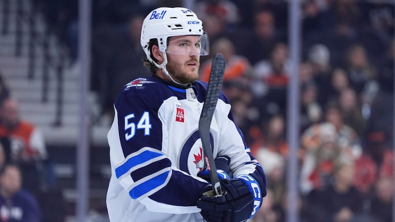 A hockey player in blue and white uniform stands up in a relaxed pose. He holds his stick off the ice.