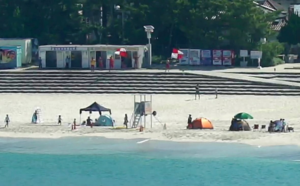 People wave red and white flags on a beach