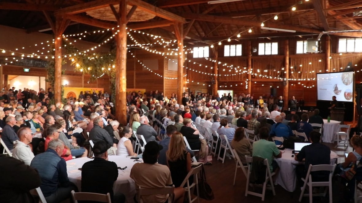Hundred of people sit in a room.
