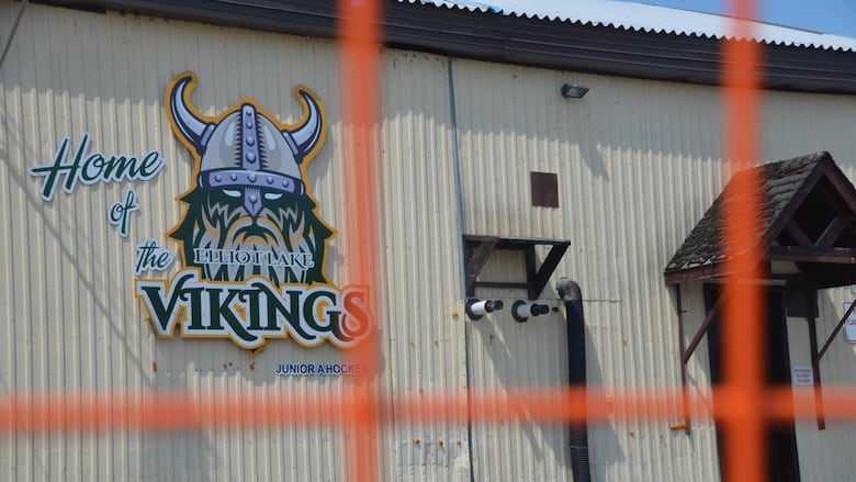 An arena wall with a picture of 'Elliot Lake Vikings' seen through a fence 