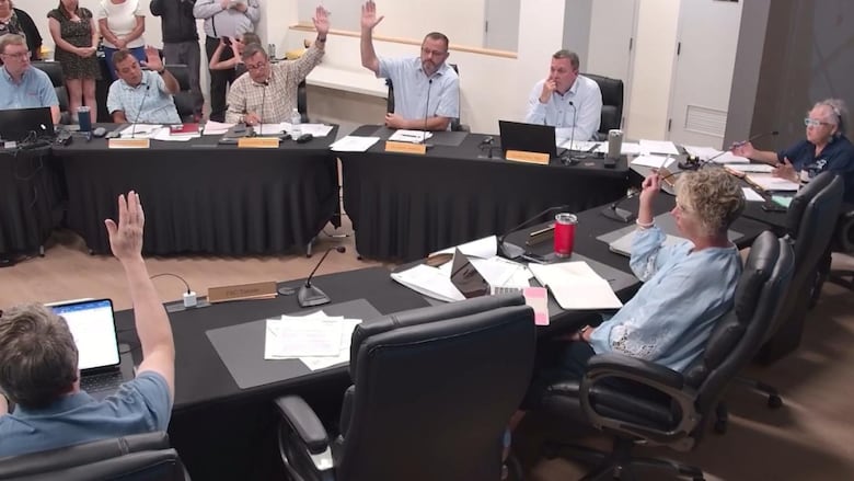 People sitting at tables raise their hands.
