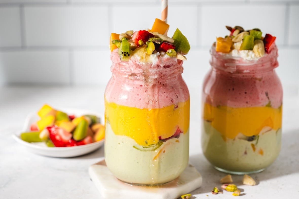 2 glass Mason jars with colourful layers of fruit smoothies in them, topped with fruit. 