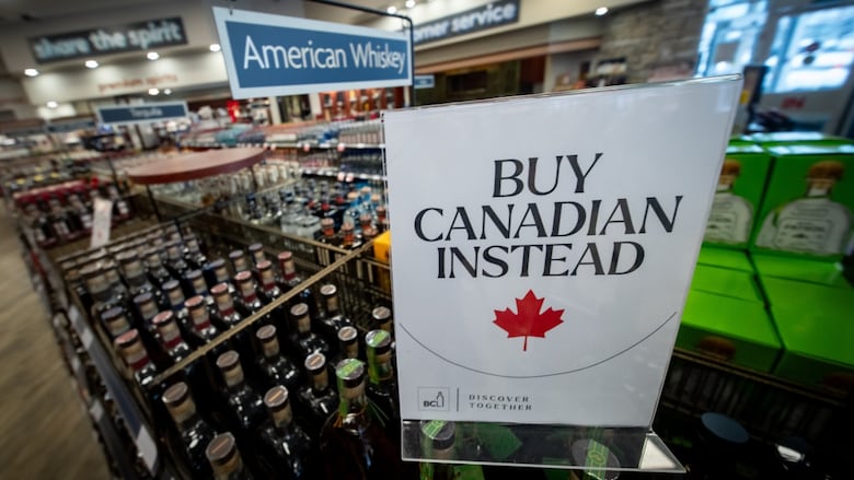 A sign in a B.C. liquor store sign sits atop bottles of Canadian whiskey reading "Buy Canadian instead" as bottles of American whiskey sit in the background.
