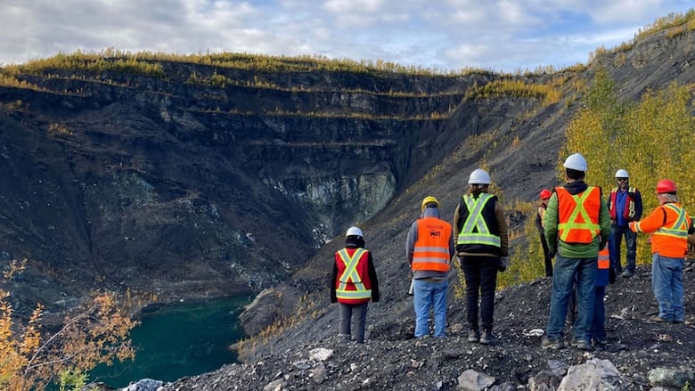People in high-vis vests stand around next to an open pit.