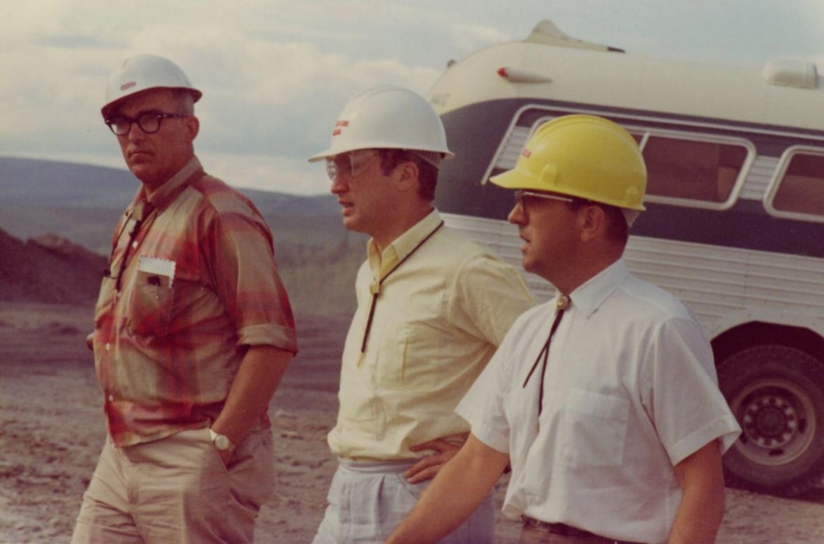 Three men in hardhats walk around outside.