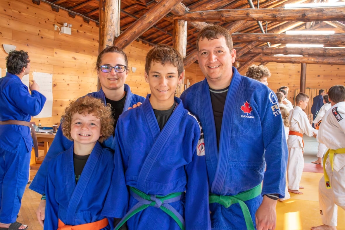 Four people are seen standing together, all wearing blue judogi. They are smiling.