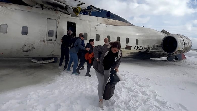 Passengers exit a crashed plane on a snowy runway.
