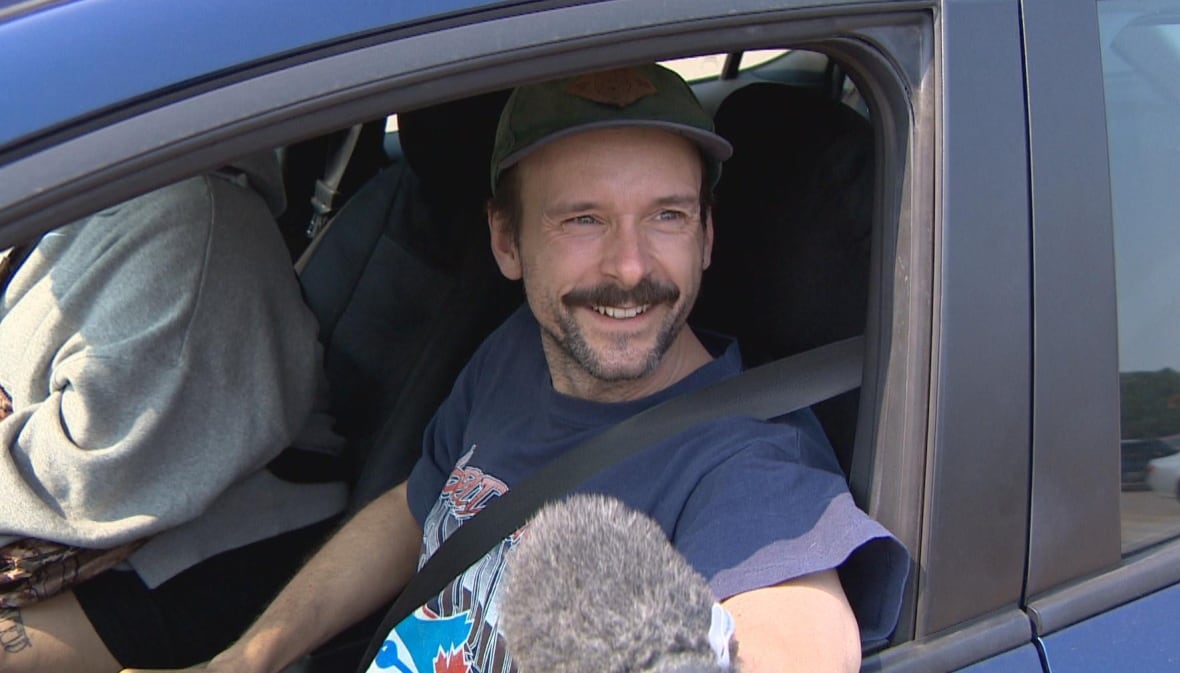 A man sitting in a car is seen being interviewed.