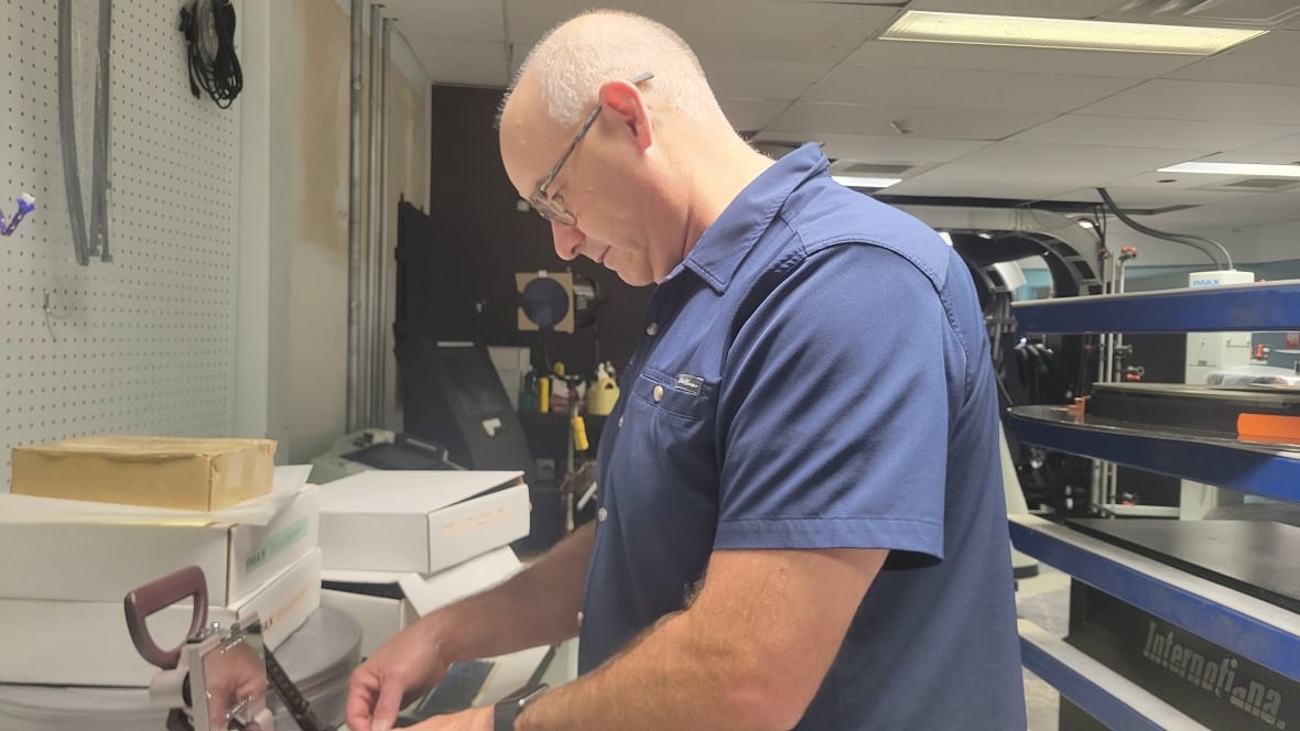 Man in a blue t-shirt cutting film.