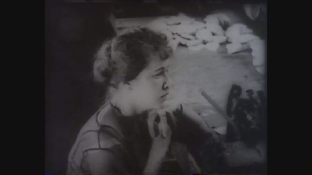 A woman slumps at a factory work table in this fuzzy black and white still.