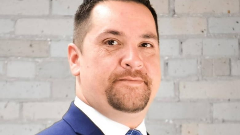 A man with dark hair is wearing a suit and looking at the camera.