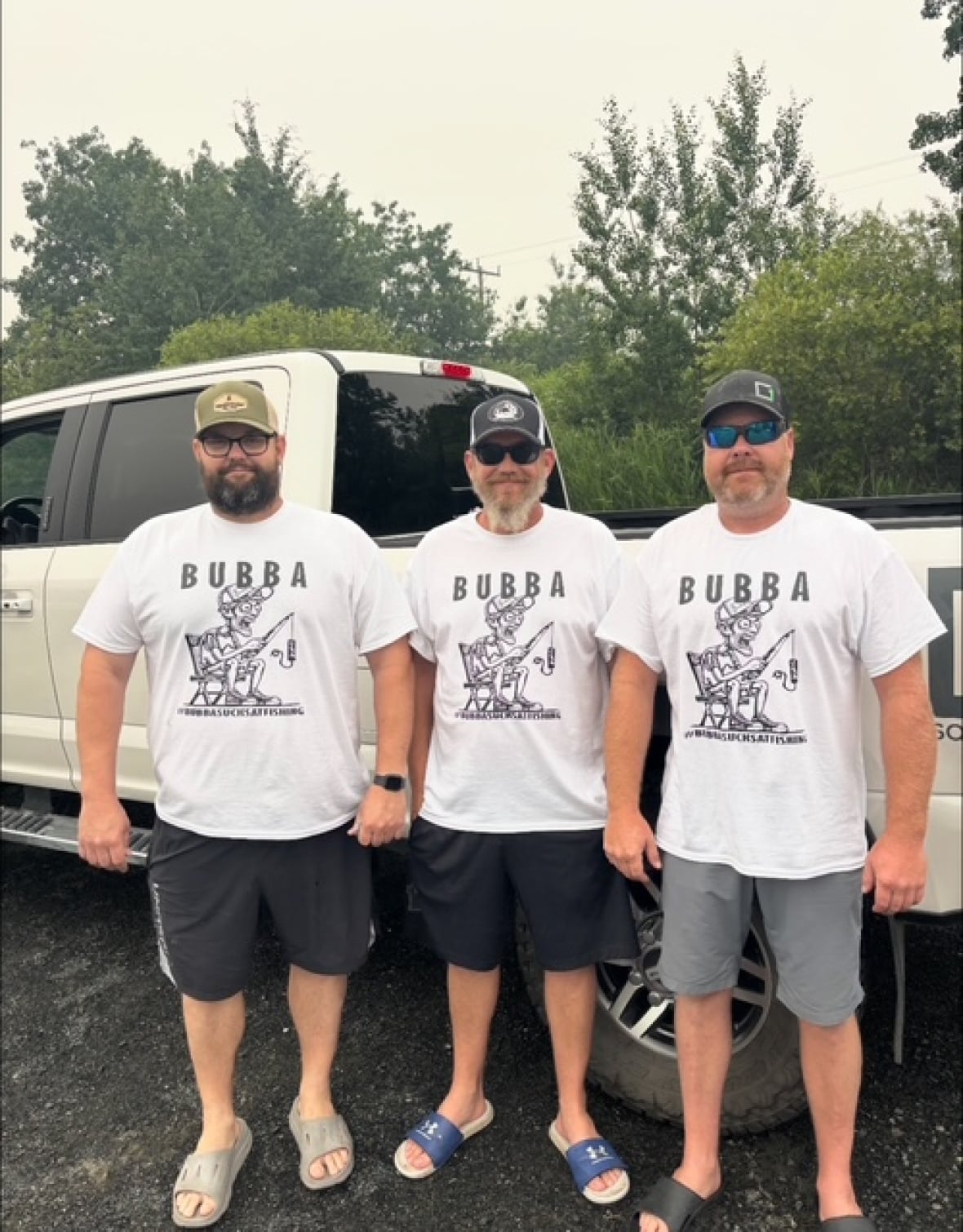 Three men wearing white t-shirts stands in front of a truck.