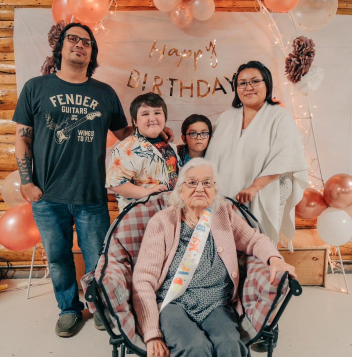 An older woman sits surrounded by family