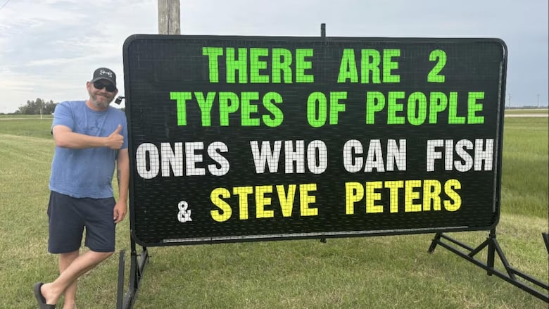 A man stands next to sign that reads: There are 2 types of people, ones who can fish and Steve Peters.