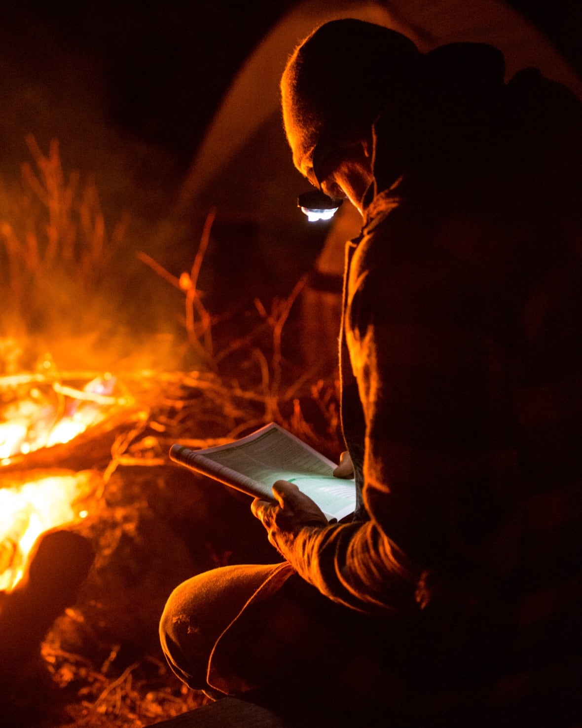 A man sits next to a campfire.