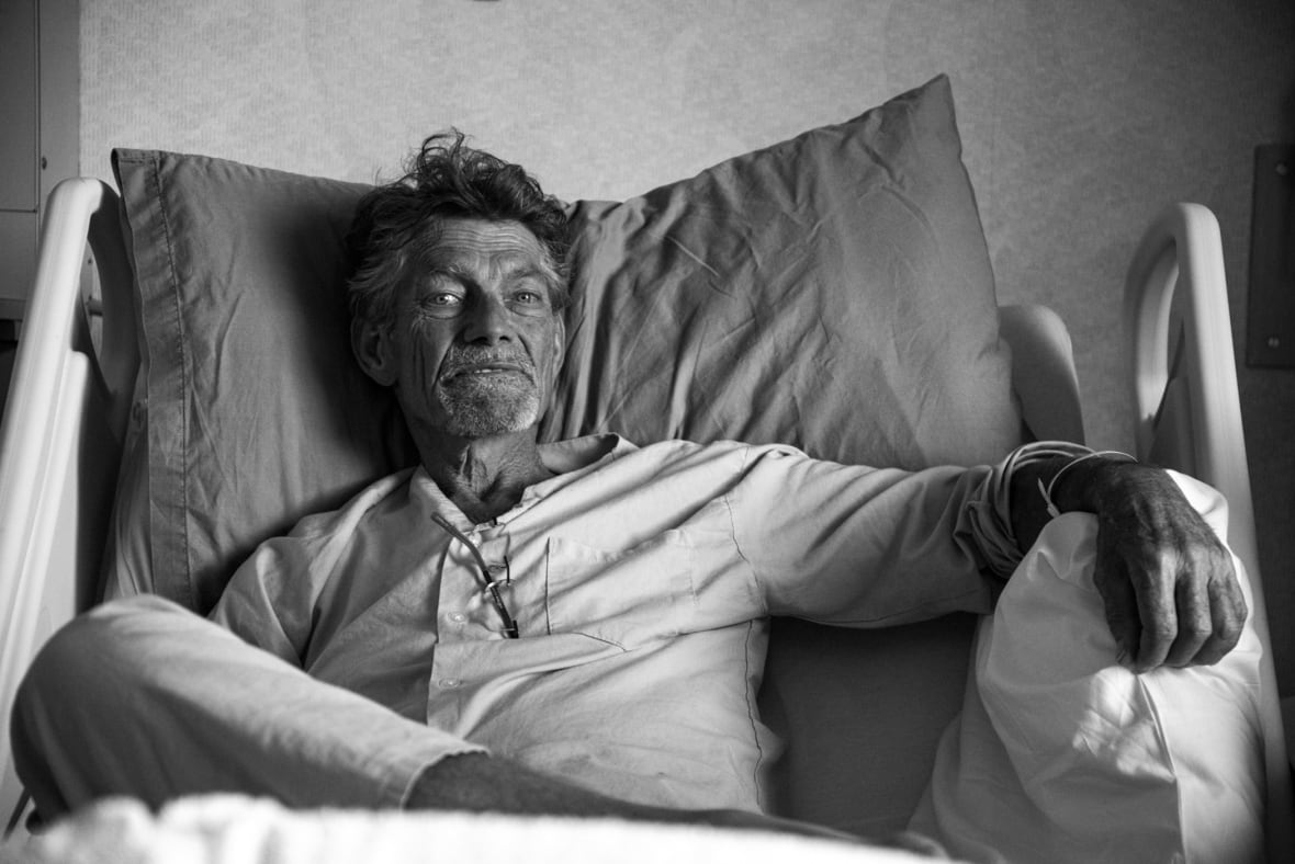 A black and white image of a man in pyjamas sitting up in a hospital bed.