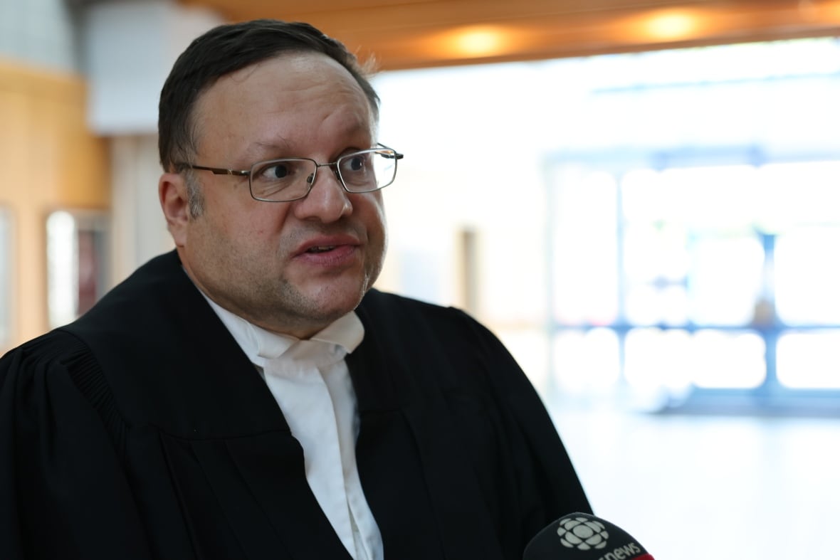 A lawyer in black and white robes looks at the camera.