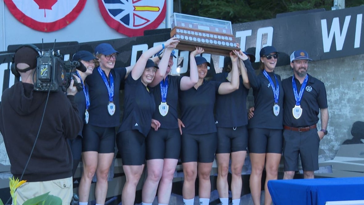 A group of women dressed in navy celebrate with a large trophy over their heads