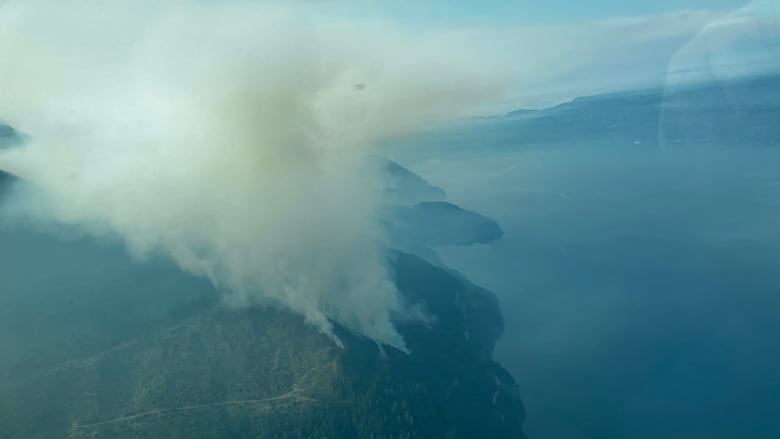 Smoke arises from a hill near a picturesque lake.