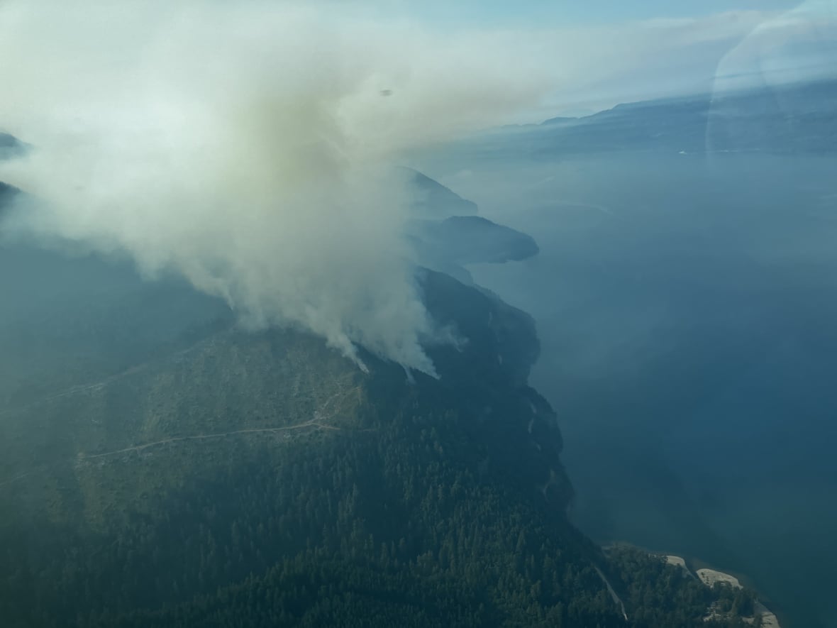 Evacuation orders expanded because of wildfire on Vancouver Island 2 Smoke arises from a hill near a picturesque lake.
