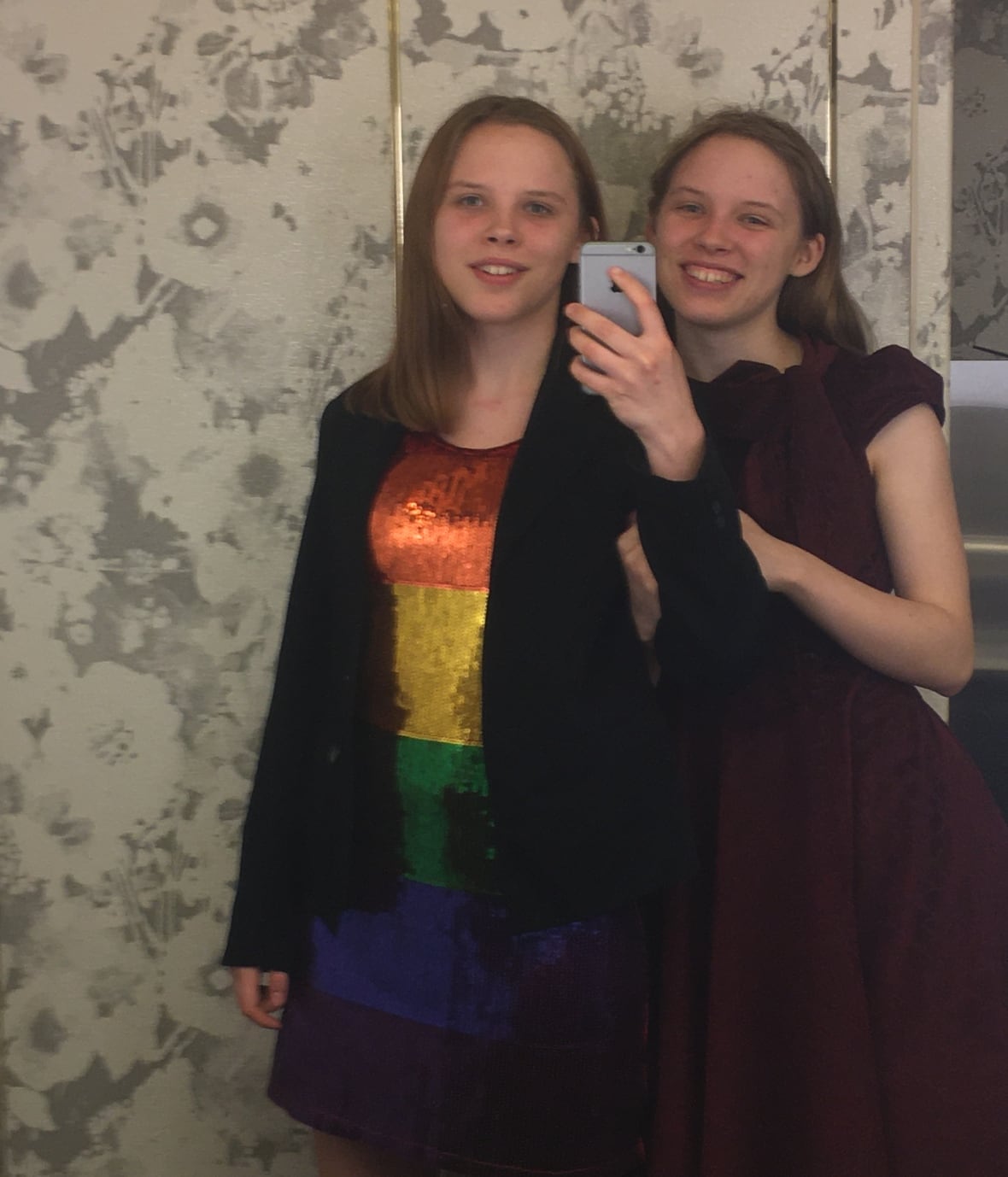 Two smiling people, one wearing a rainbow-coloured dress and the other wearing a vintage dress, pose for a photo. 