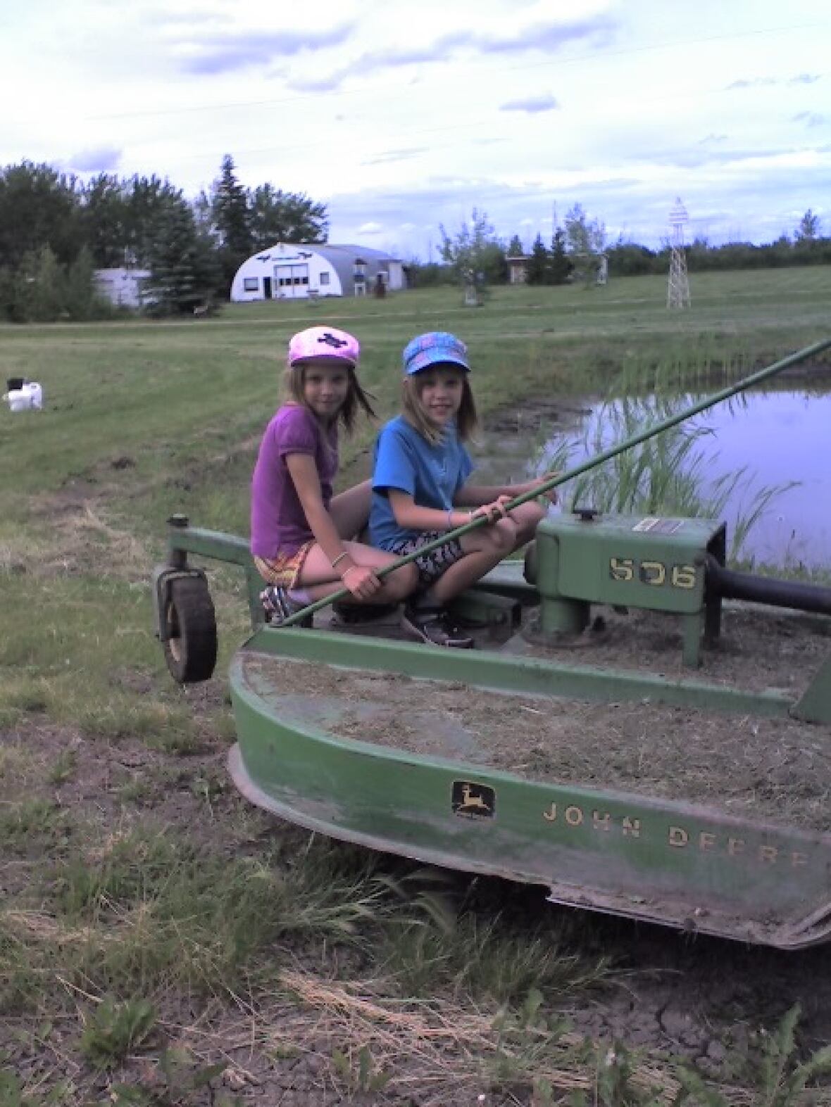 Two identical twin girls sit in a rotary mower. 
