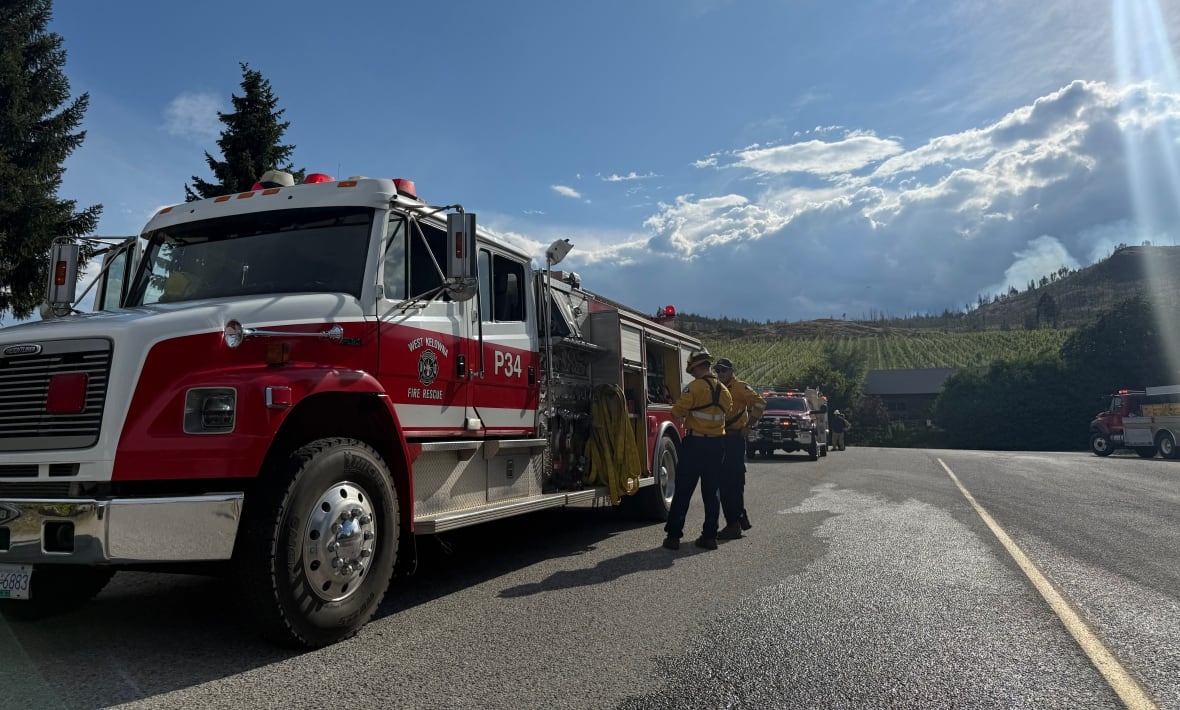 Firefighters stand next to a fire truck on a sunny day.
