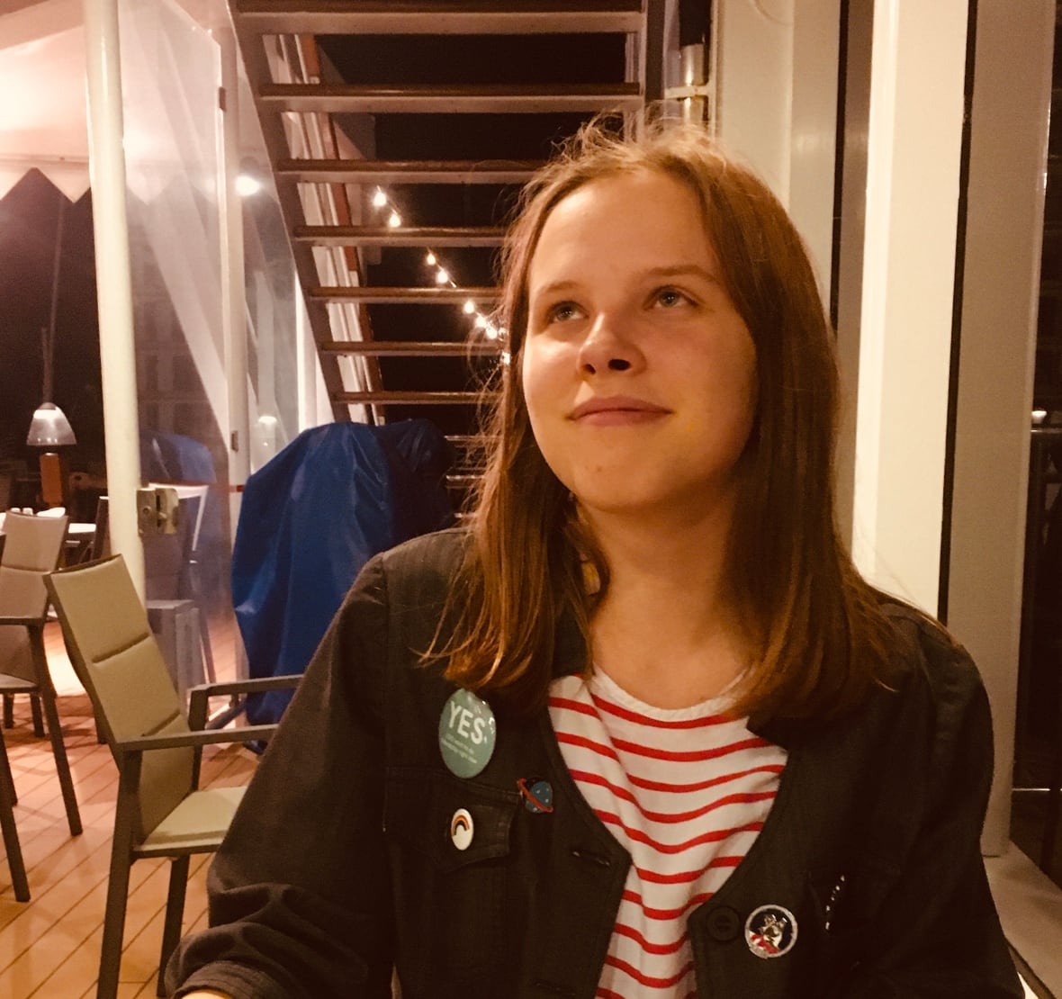 A person with shoulder-length hair looks up while sitting at a table in front of a pizza. 