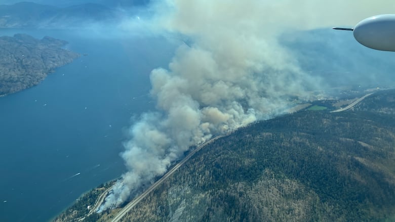 Smoke arises from a fire burning next to a large lake and two highways.
