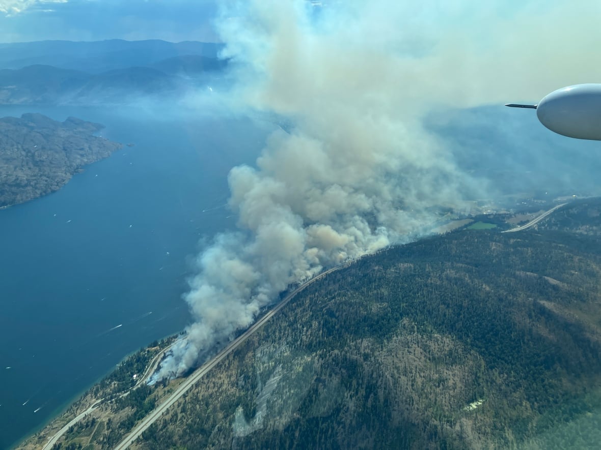 The smoke arises from a burning fire next to a large lake and two roads.