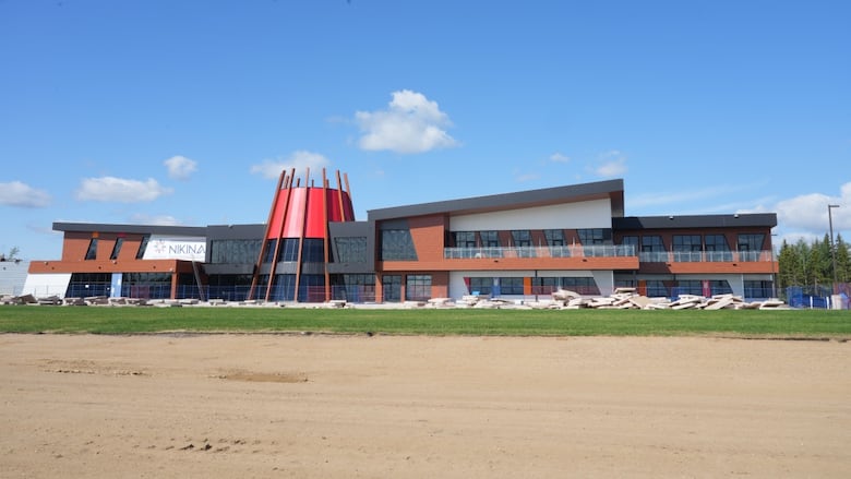 Wide shot of a building, with a large red-tipped teepee-like structure in the middle of it. Beach in the foreground. 