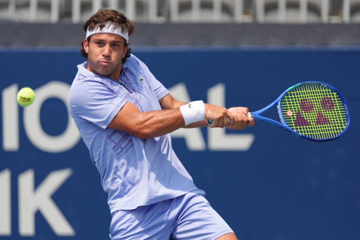 A man in a blue shirt and shorts aims for the tennis ball with his racket.