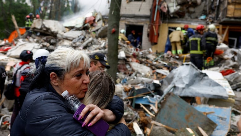 A woman embraces another woman in front of the site of an airstrike at an apartment building.