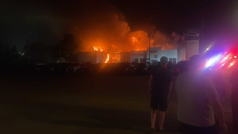 Flames shoot up from a car dealership at nighttime. 