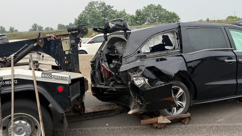 A black van that has been badly damaged is hooked up to a tow truck.