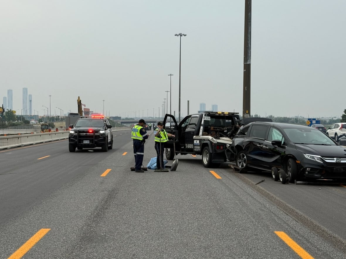 Police investigate a motor vehicle collision on a highway. Two police officers can be seen looking at a vehicle that is damaged and hooked up to a tow truck.