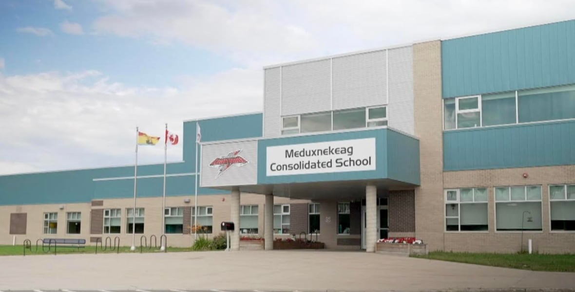 An exterior shot of a building with the name Meduxnekeag Consolidated School on the entrance wall, in summer.