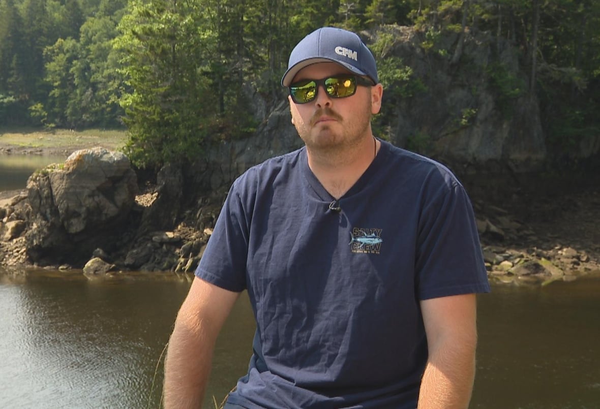 A man wearing sunglasses and a blue hat sitting in front of a shoreline