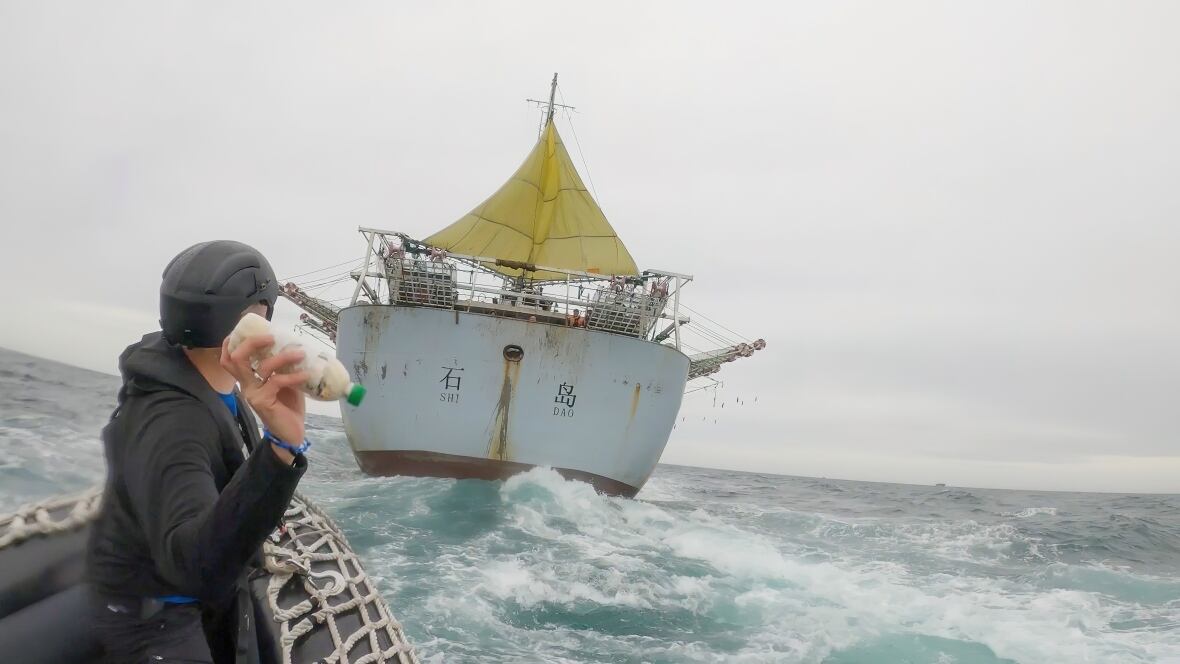An action shot of a man throwing a bottle from a small dinghy onto a fishing vessel on the rough ocean.